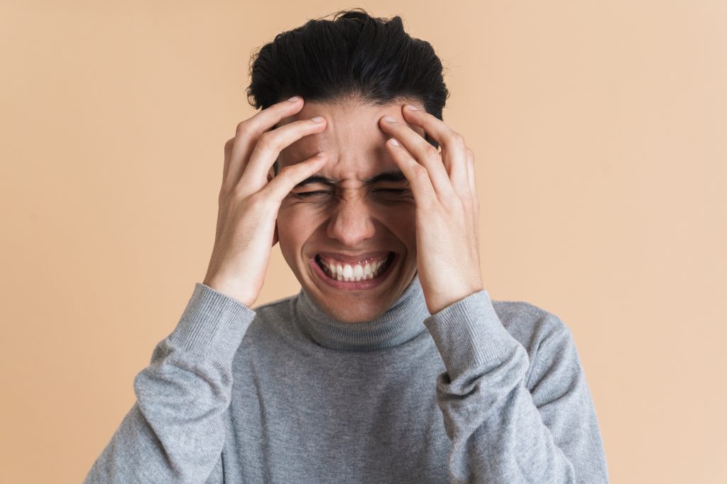 young man grimacing while holding head looking stressed